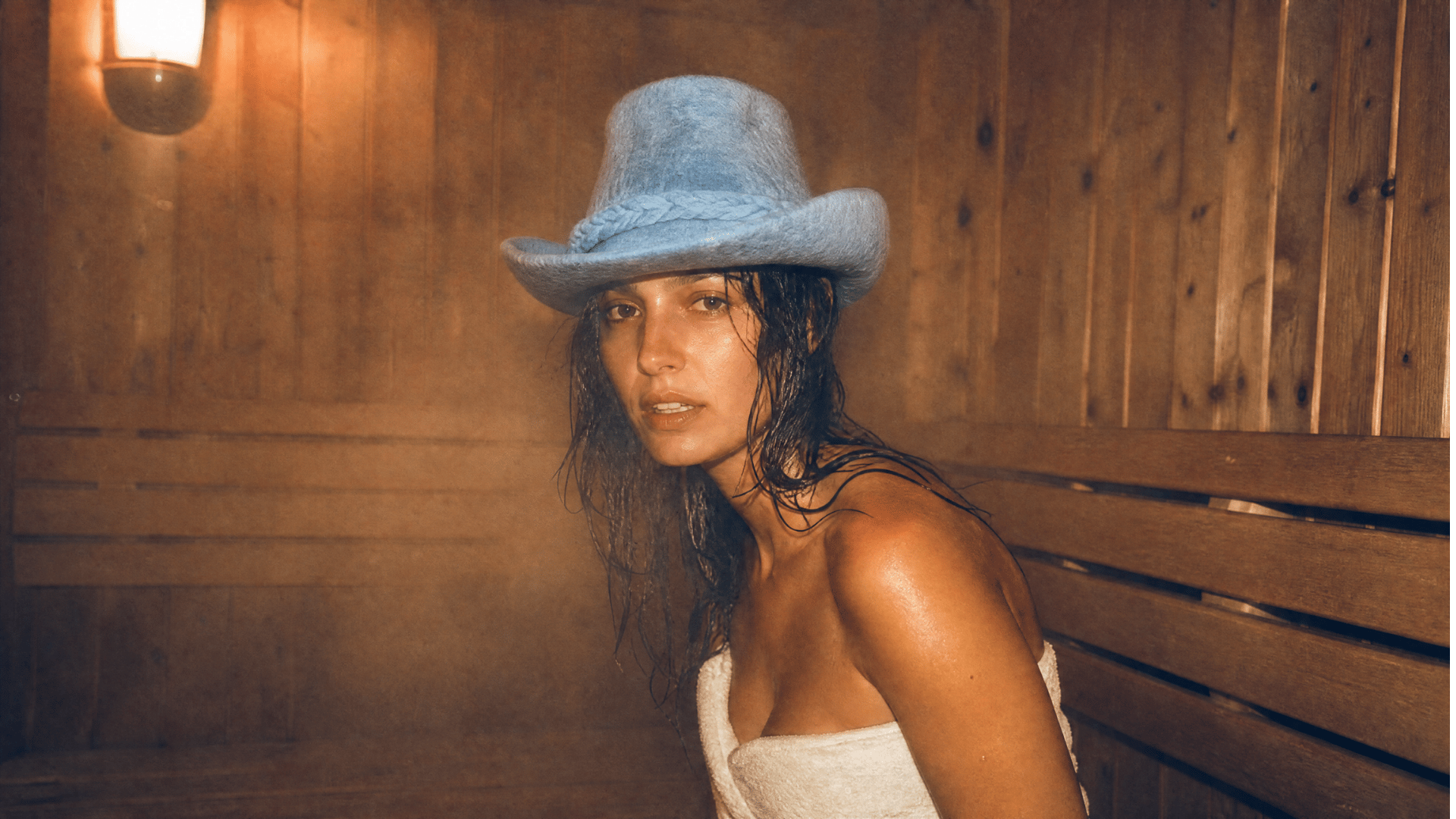 A model wearing the löyl cowboy sauna hat in naturally dyed blue wool felt by a pool