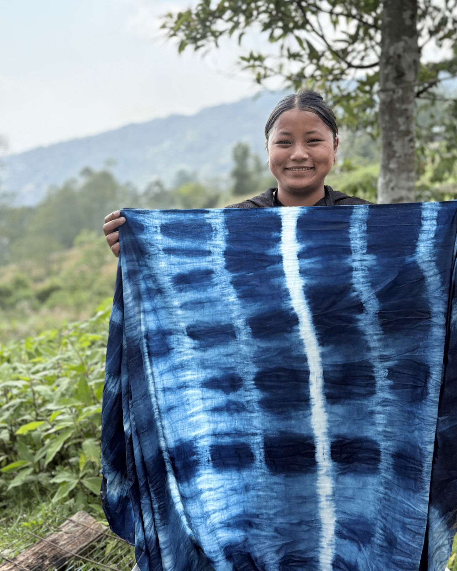 Artisan in Nepal holding up a length of hand-dyed indigo shibori cloth